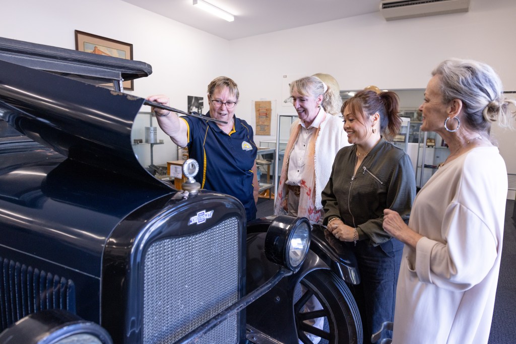 A group of ladies and a museum volunteer looking at the engine of a vintage car
